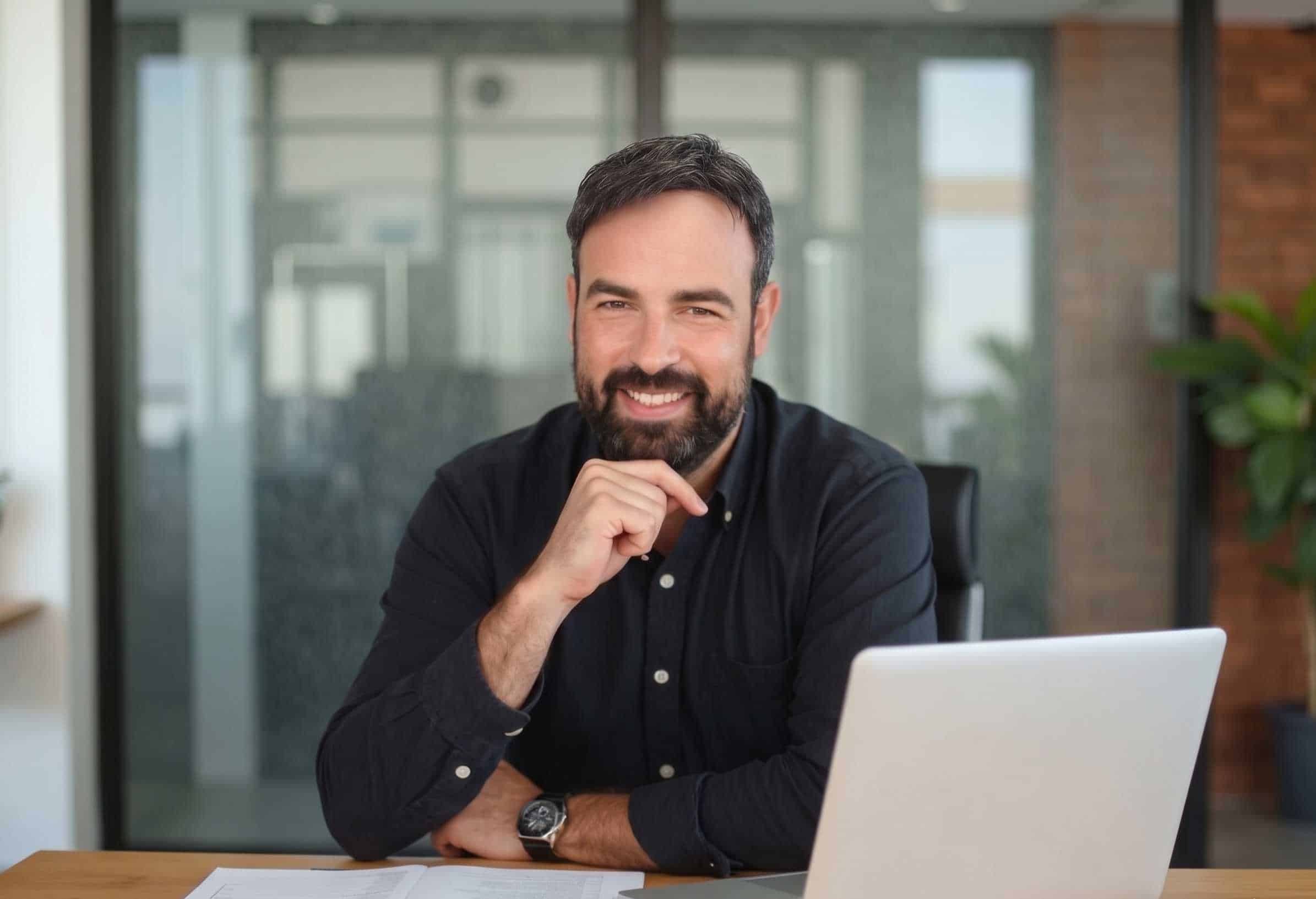 Man in the office on a call, smiling, with laptop and notepad.